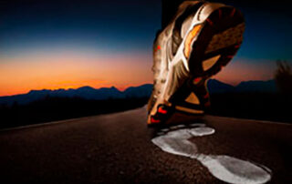 Zapatilla de un corredor en el asfalto que deja la huella de un pie descalzo.